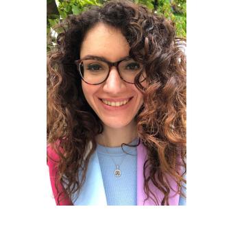 Curly hair and glasses. Purple jacket, light blue t-shirt.